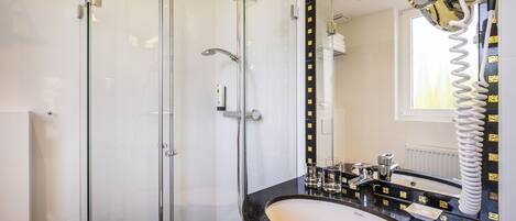 Een moderne badkamer met een douchecabine van glas, een zwart marmeren wastafel en een grote spiegel met een gouden lijst.