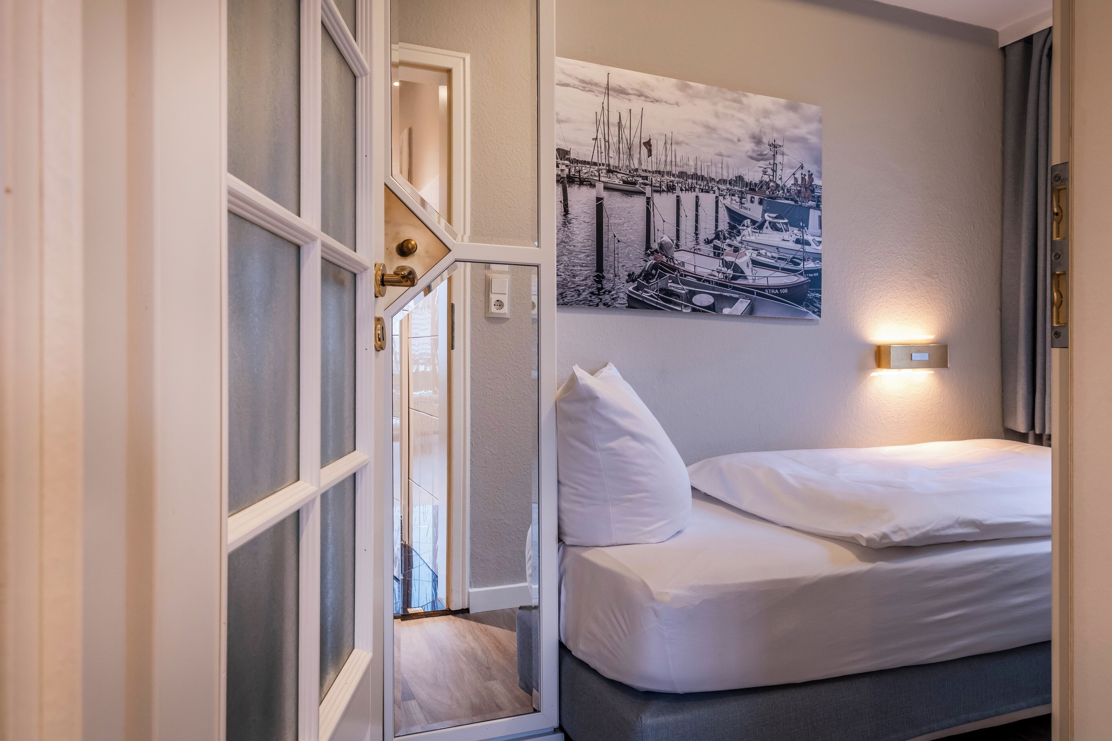 Ein Hotelzimmer mit Bett, einem Hafenbild und einer Tür mit Blick auf einen Balkon.