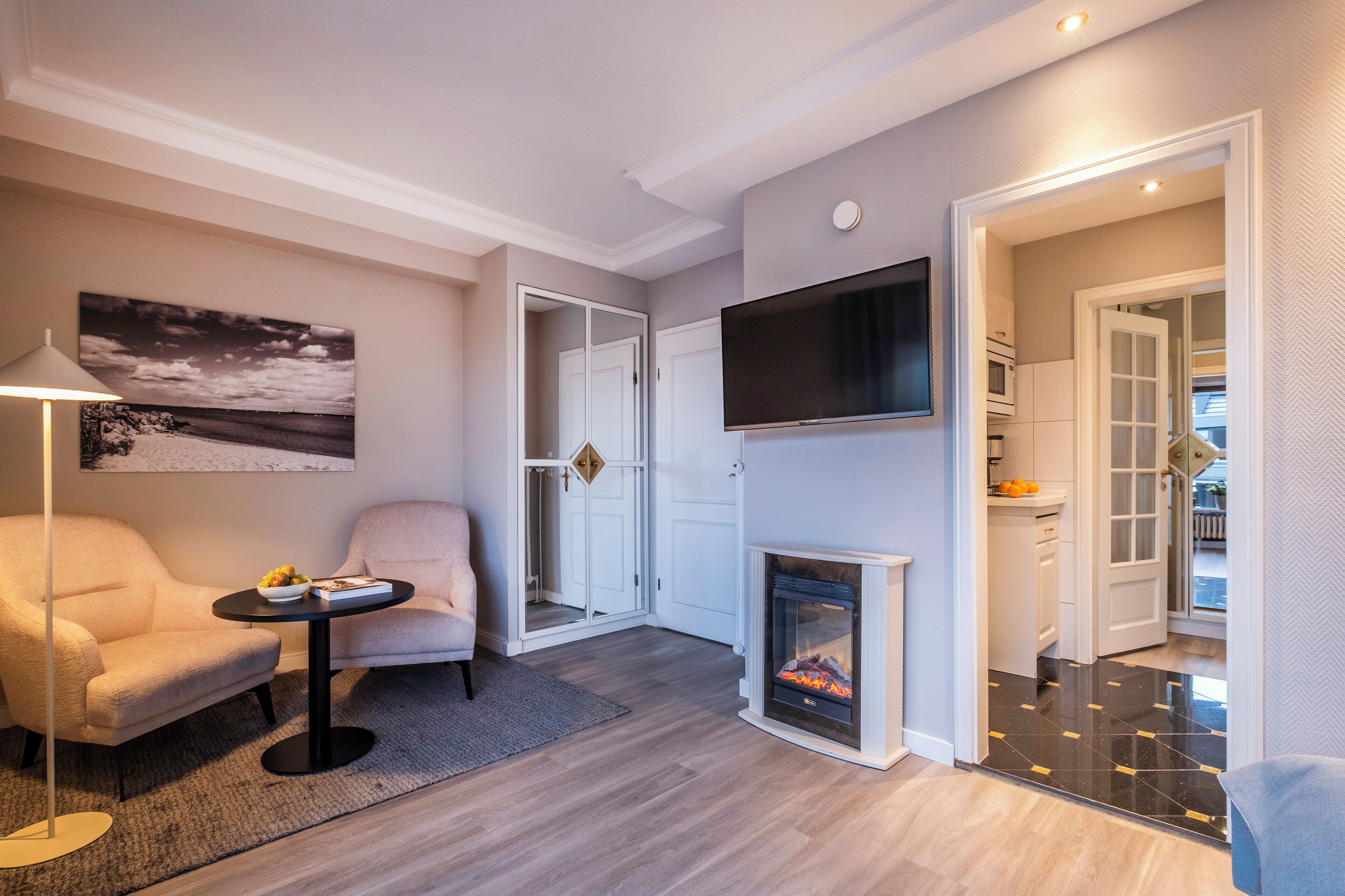 Ein modernes Wohnzimmer mit Kamin, Flachbildfernseher an der Wand und einer gemütlichen Sitzecke mit Lampe und Sessel.