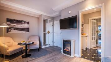 Ein modernes Wohnzimmer mit Kamin, Flachbildfernseher an der Wand und einer gemütlichen Sitzecke mit Lampe und Sessel.