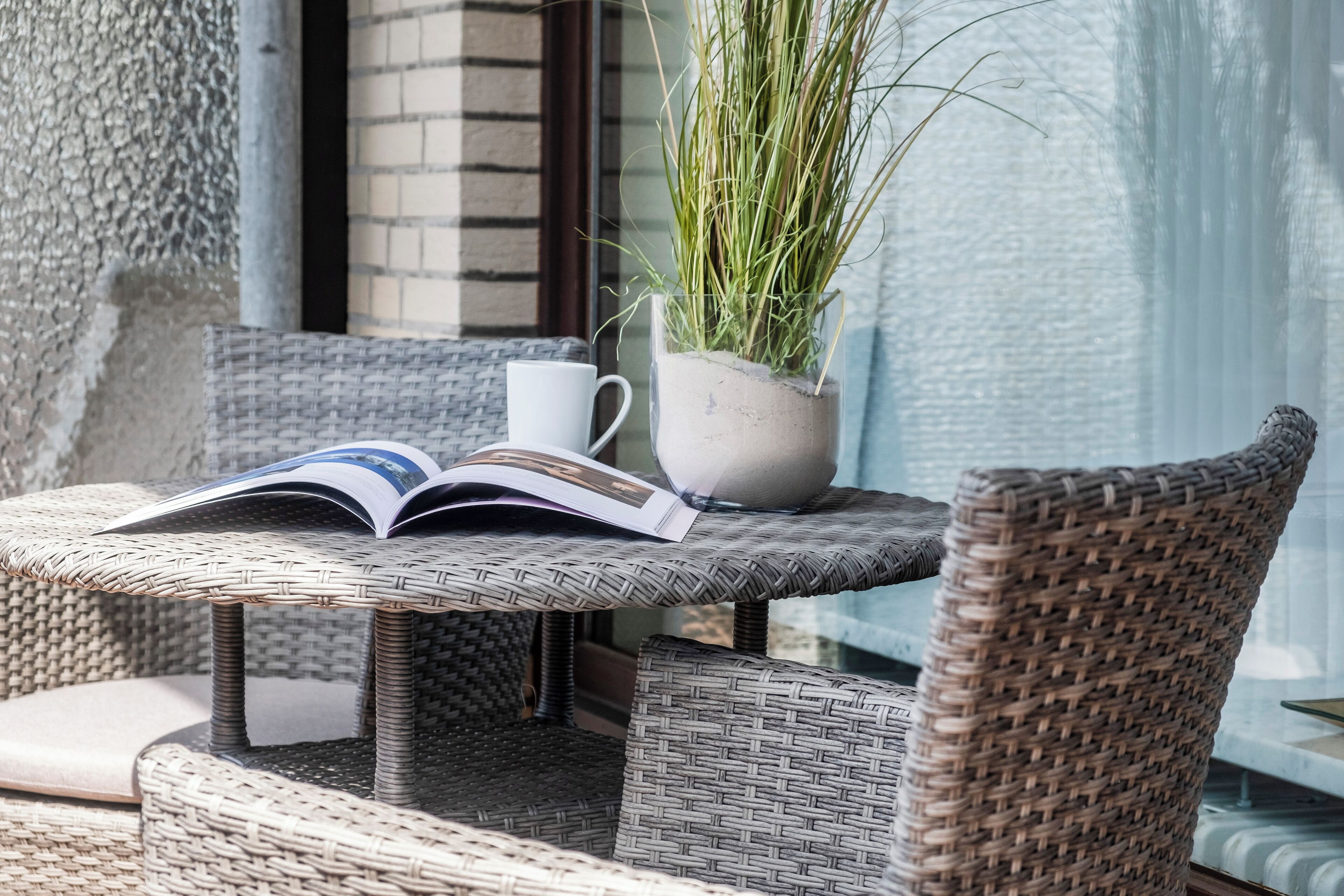A wicker chair and table with a book and a potted plant.