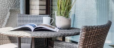 A wicker chair and table with a book and a potted plant.