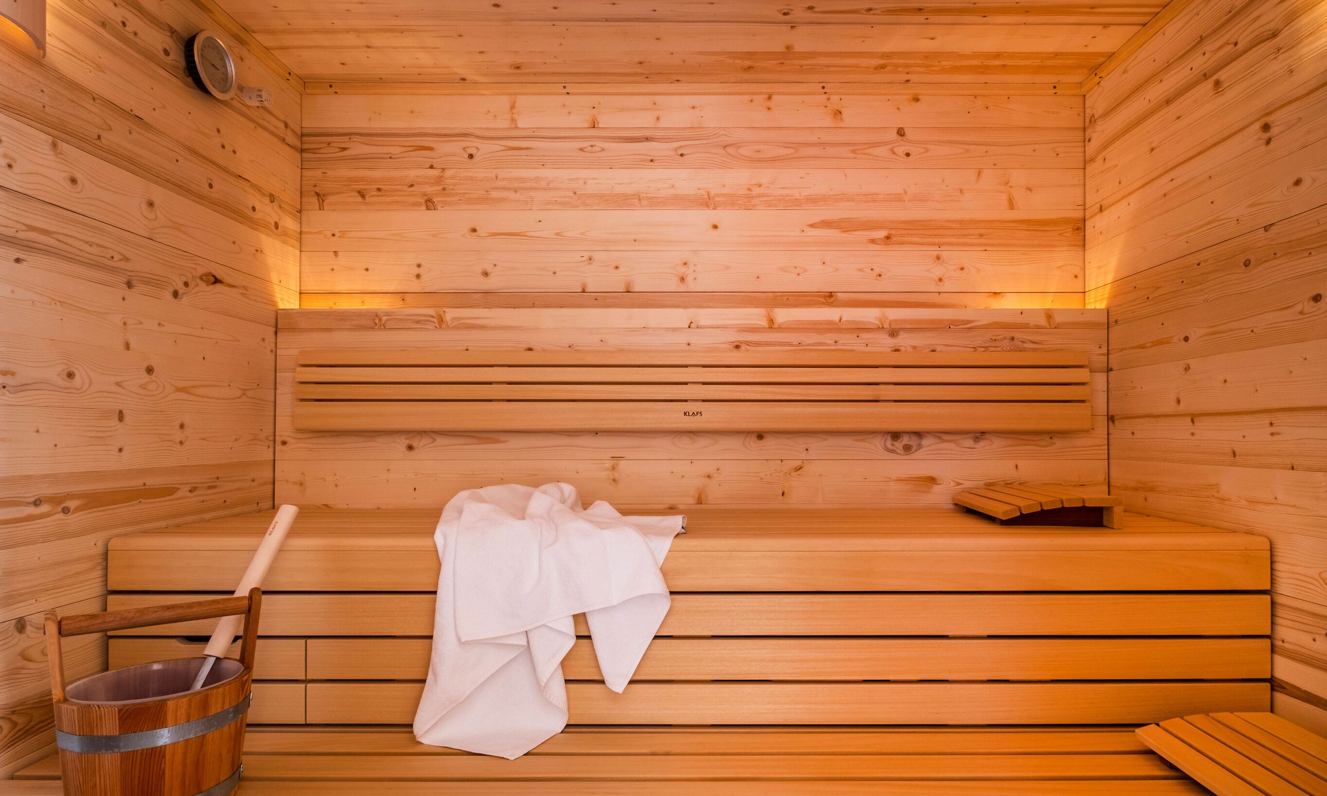 A wooden sauna with benches, a towel, and a bucket.