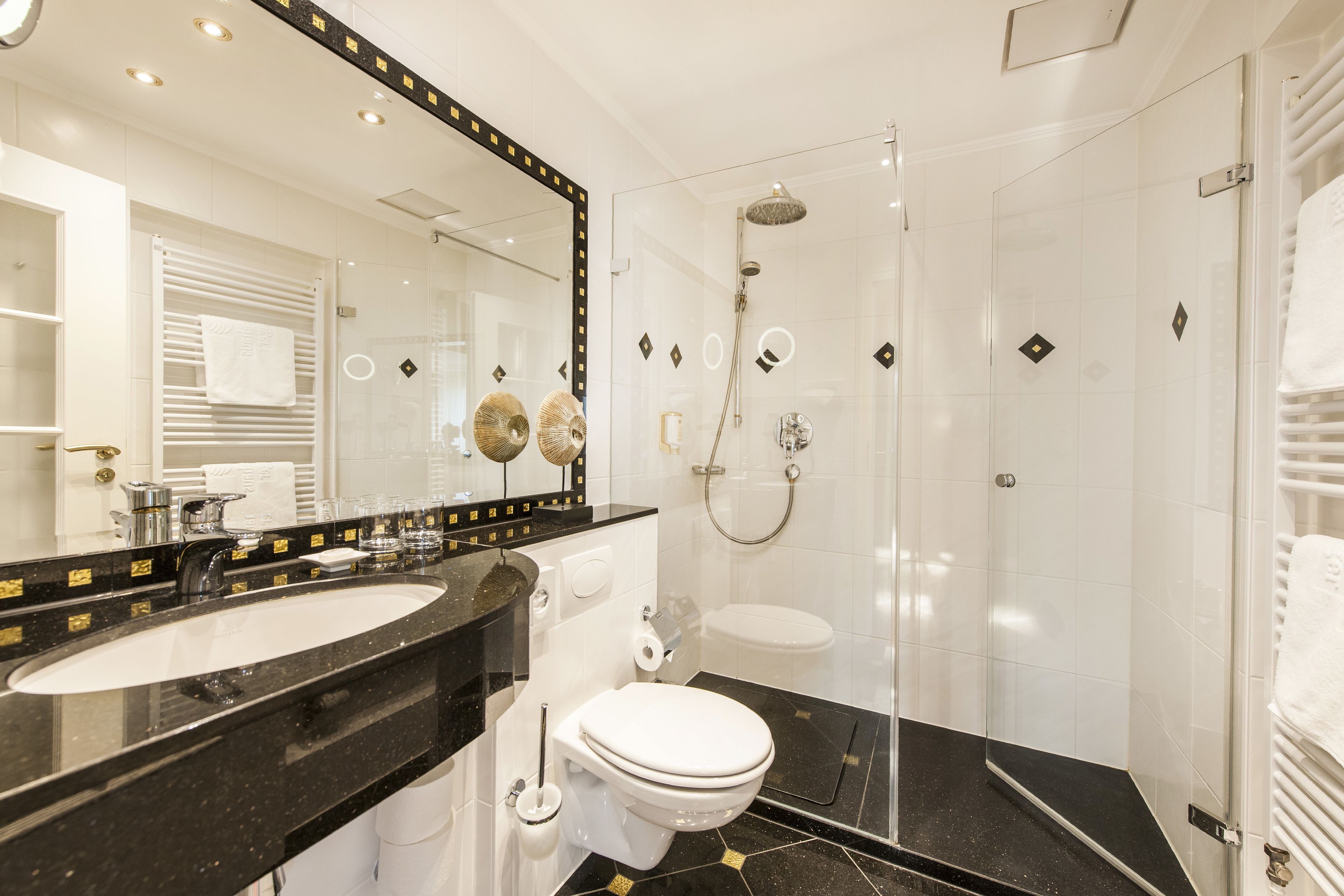 Une salle de bain moderne avec un lavabo en marbre noir, des toilettes blanches et une douche à parois de verre.