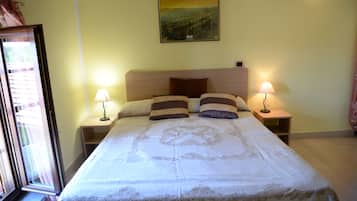 A neatly made bed with a headboard, two bedside tables with lamps, a painting on the wall, and a window with curtains.