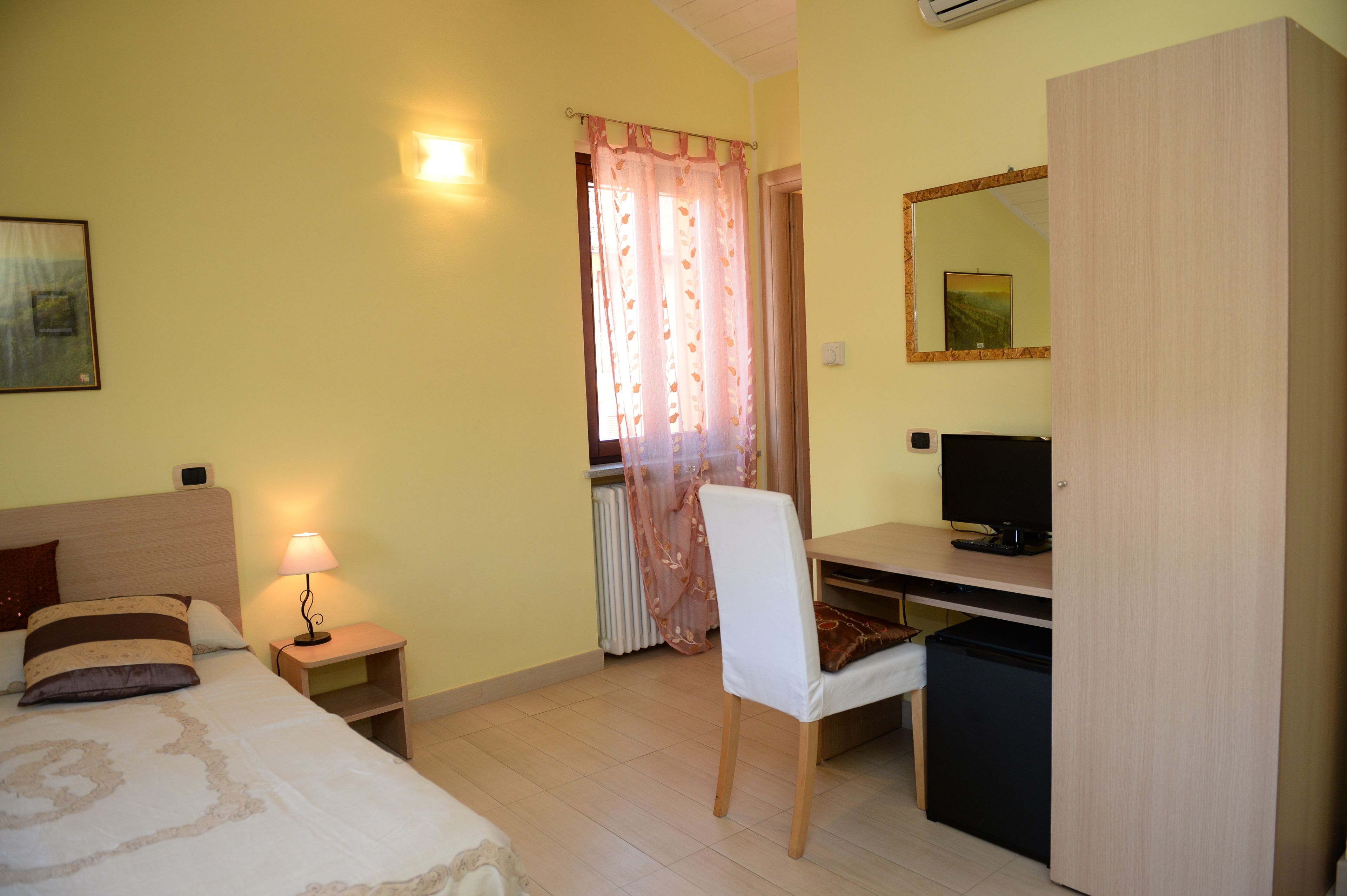 A bedroom with a bed, bedside lamp, chair, desk, TV, and wardrobe.