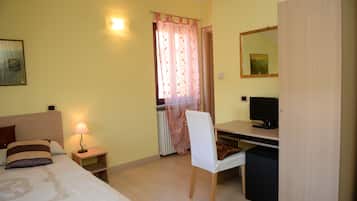 Quarto com cama, luminária de cabeceira, cadeira, escrivaninha, televisão e guarda-roupa.