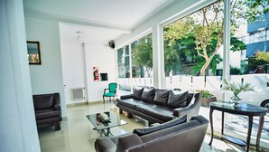 A modern living room with a sectional sofa, a glass coffee table, and a view of the outdoors through large windows. - Hotel Pelayo (Mar del Plata)