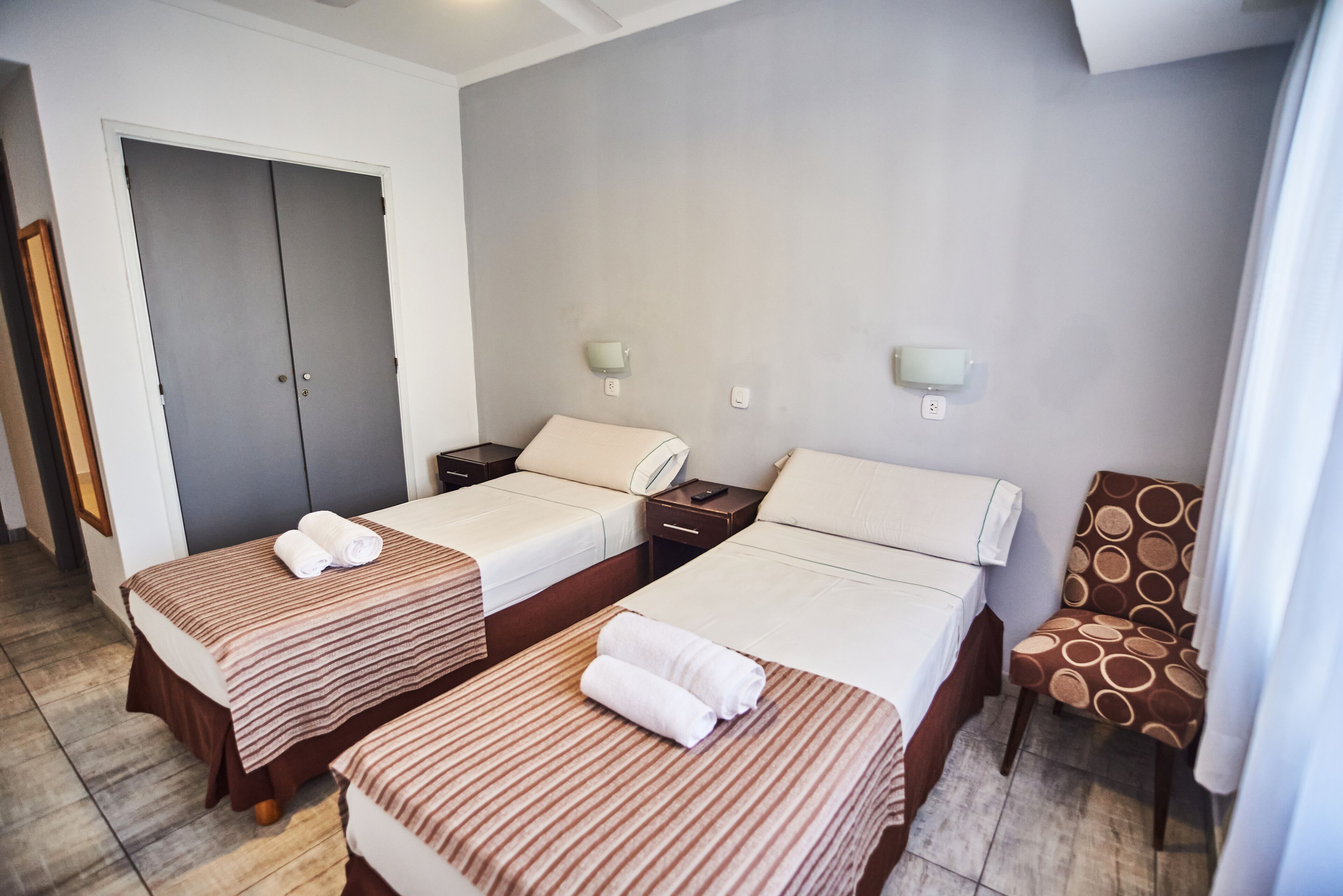 A hotel room with two single beds, a chair, a desk, and a wardrobe.