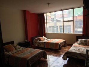 Habitación de hotel con dos camas, una pared de acento roja y un ventanal con vistas a edificios.