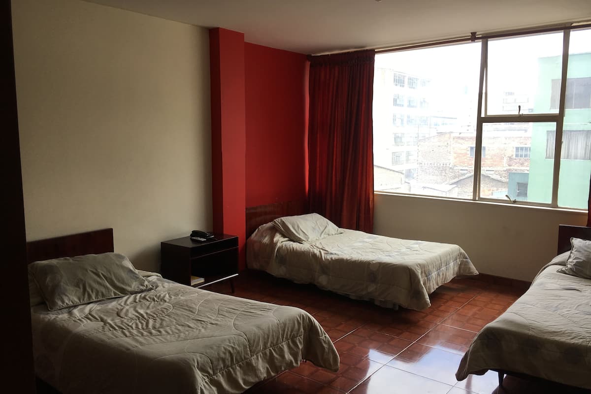 A hotel room with two beds, a nightstand, and a window with a view of buildings.