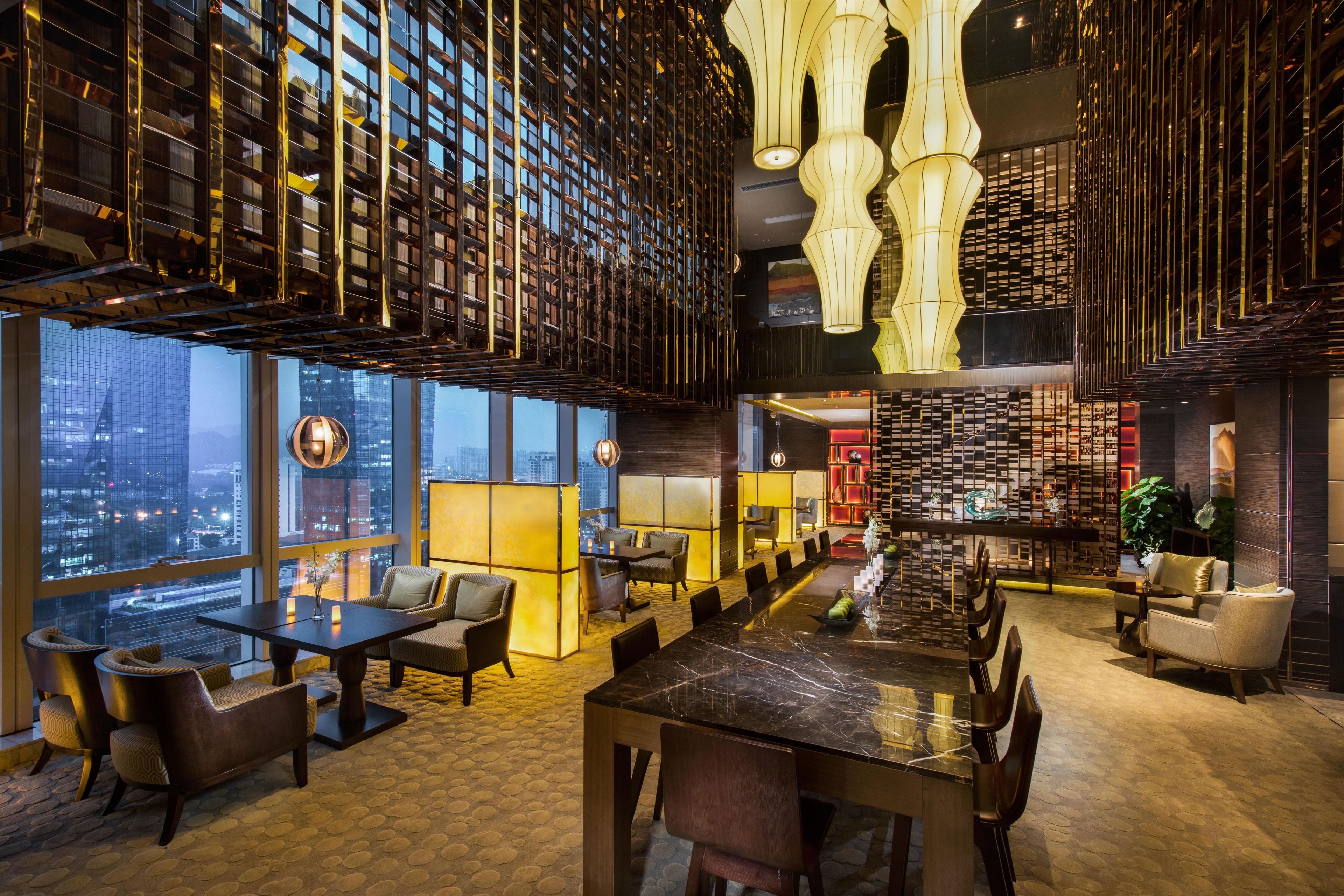 A modern hotel lobby with a large dining table, comfortable seating, and a city view.