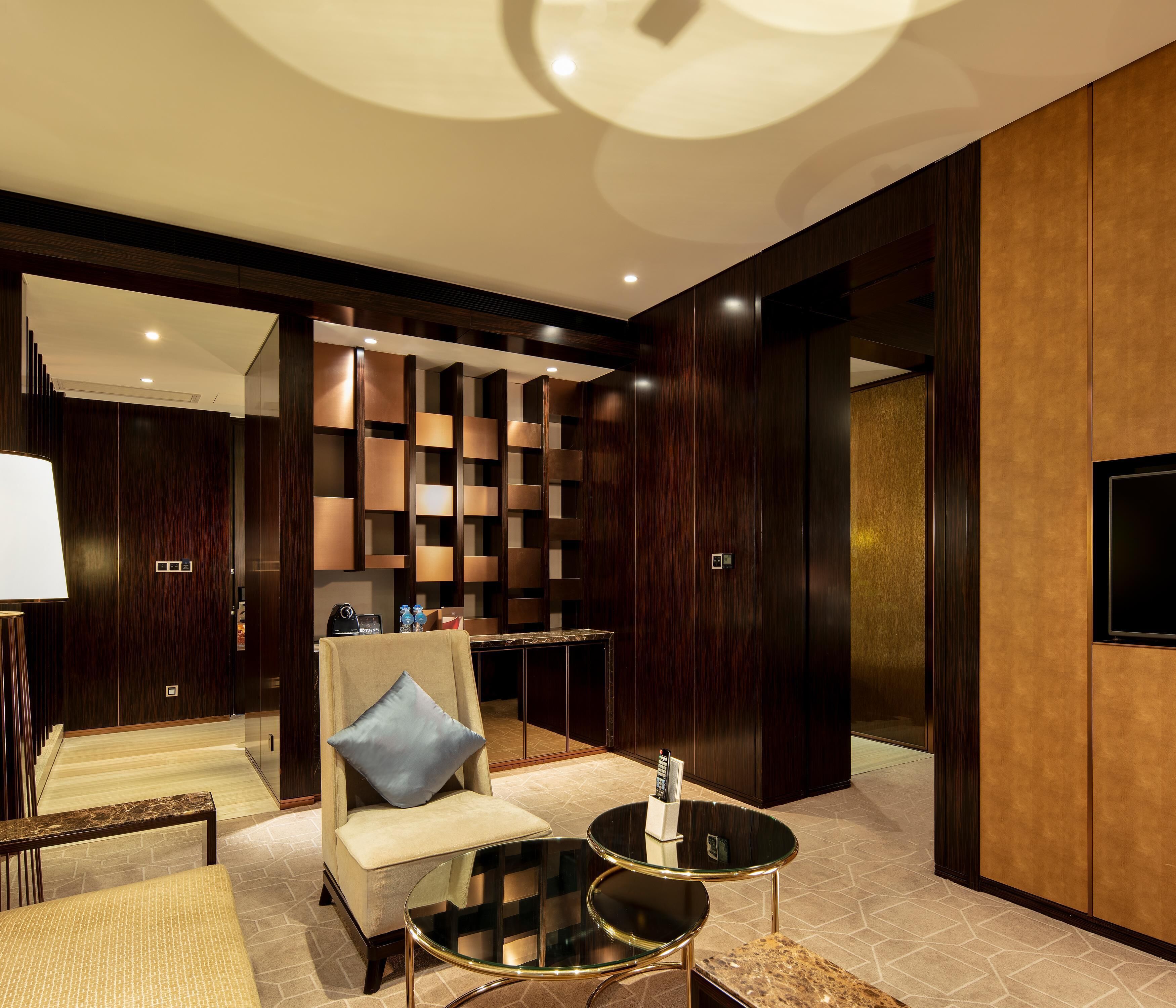 A modern hotel lobby with a seating area, a glass coffee table, and a wall-mounted TV.