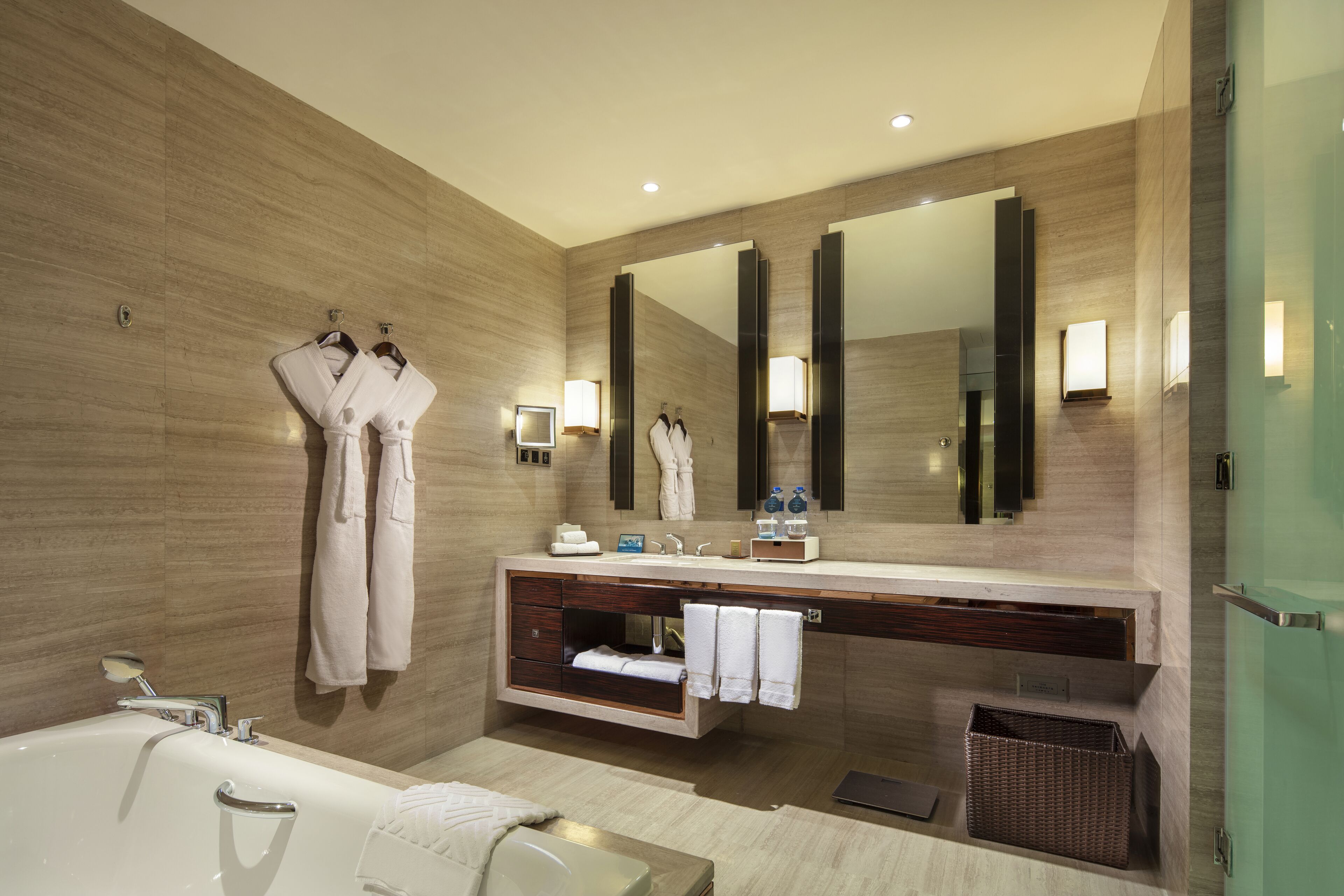 A modern bathroom with a large mirror, a bathtub, a vanity with a sink, and two robes hanging on hooks.