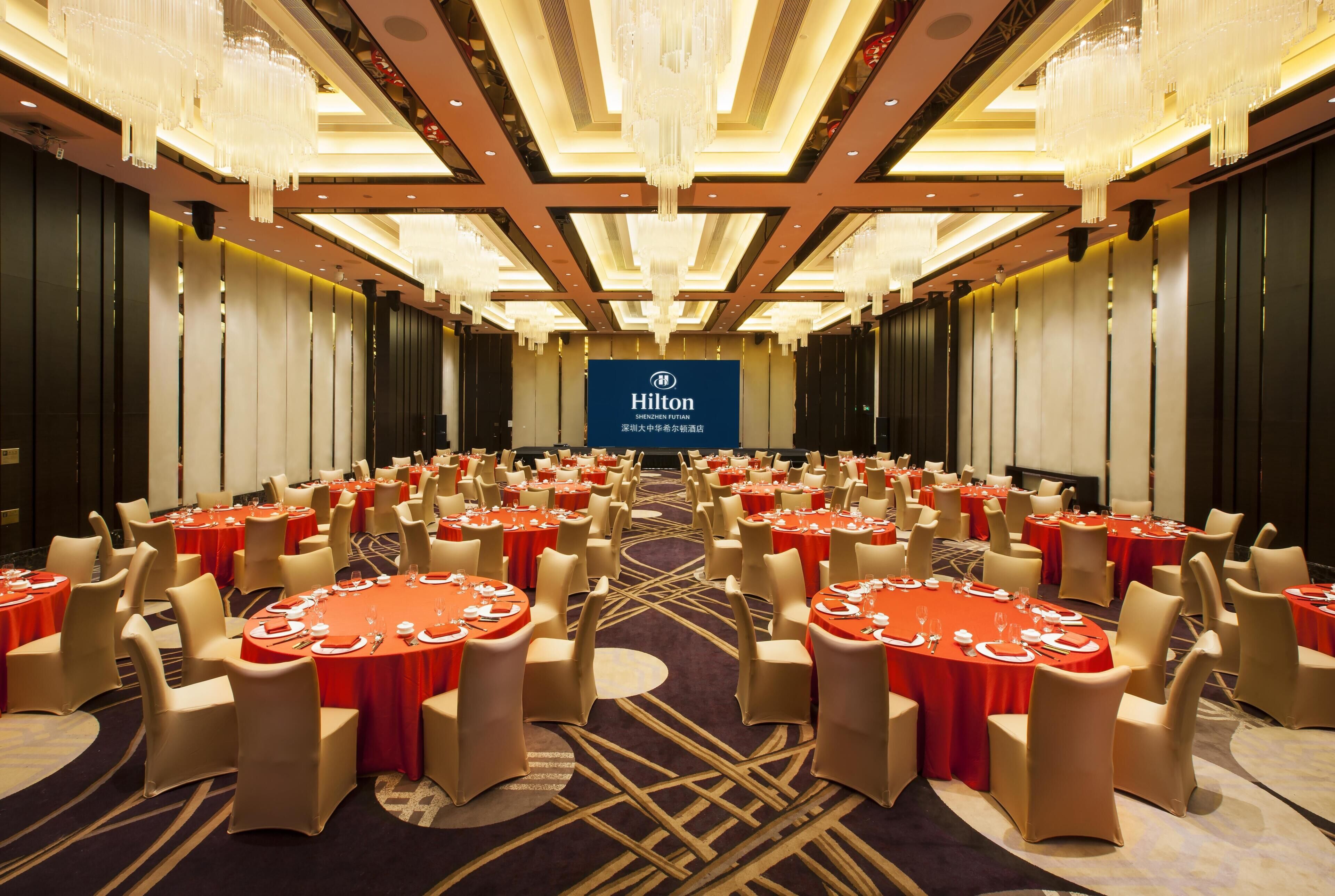 A large conference room with round tables, beige chairs, and a Hilton logo on the wall.
