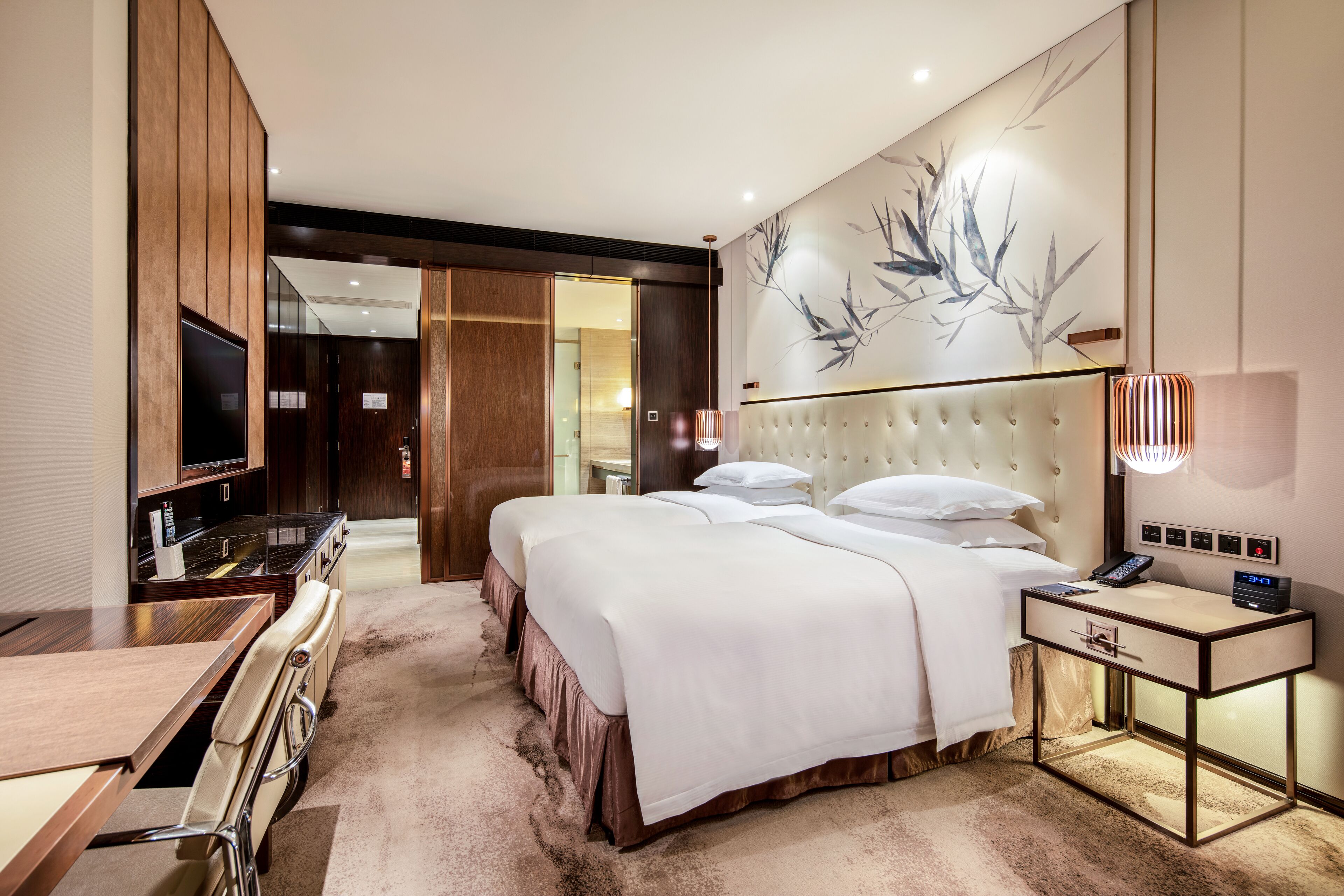A modern hotel room with a large bed, a desk, a television, and a bathroom visible through an open door.