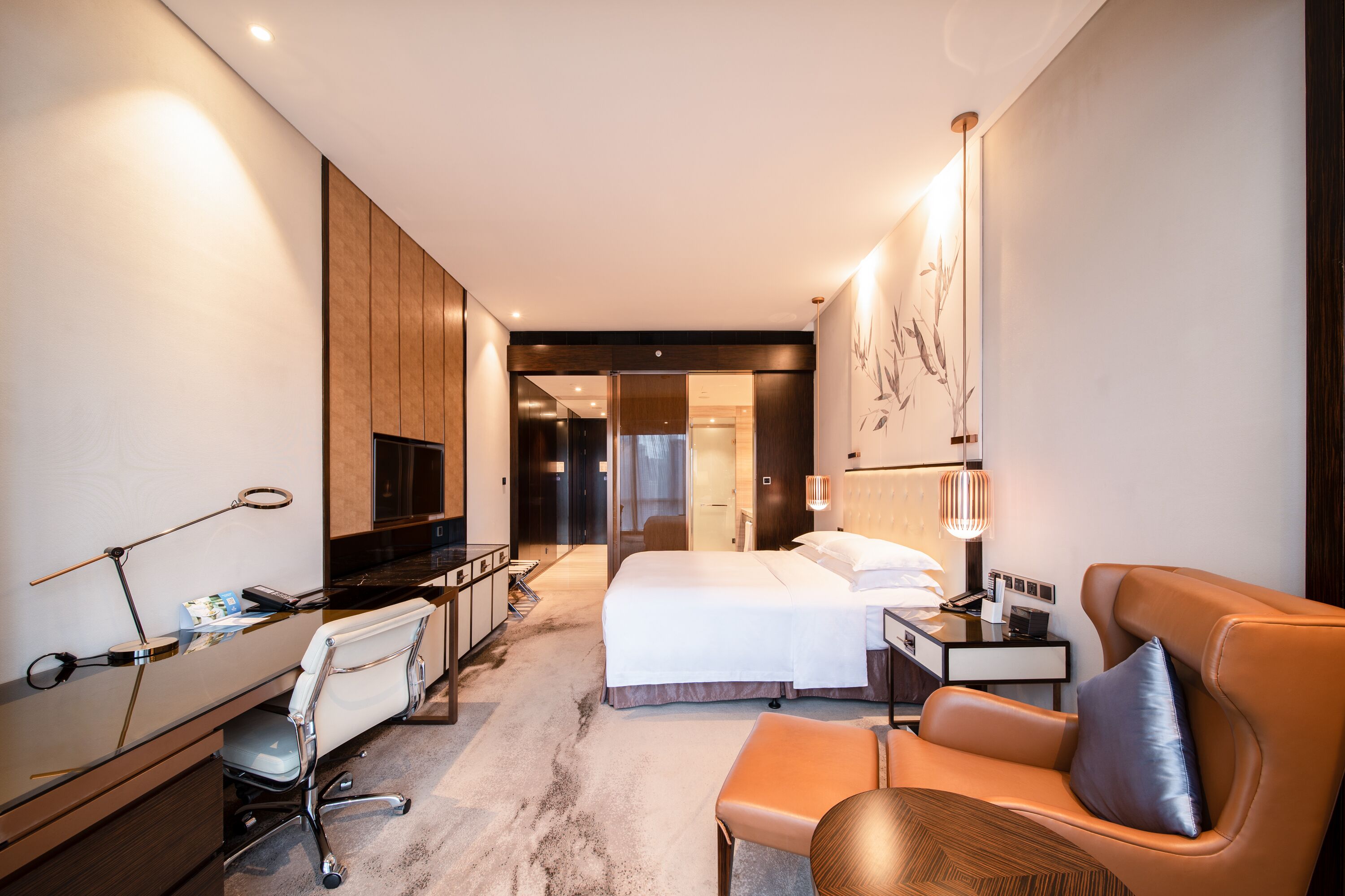 A modern hotel room with a bed, desk, chair, and a small table.