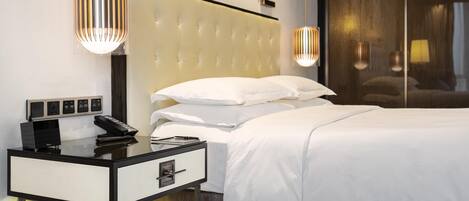 A modern hotel room with a tufted headboard, a bedside table with a phone and a lamp, and a large window with a view.