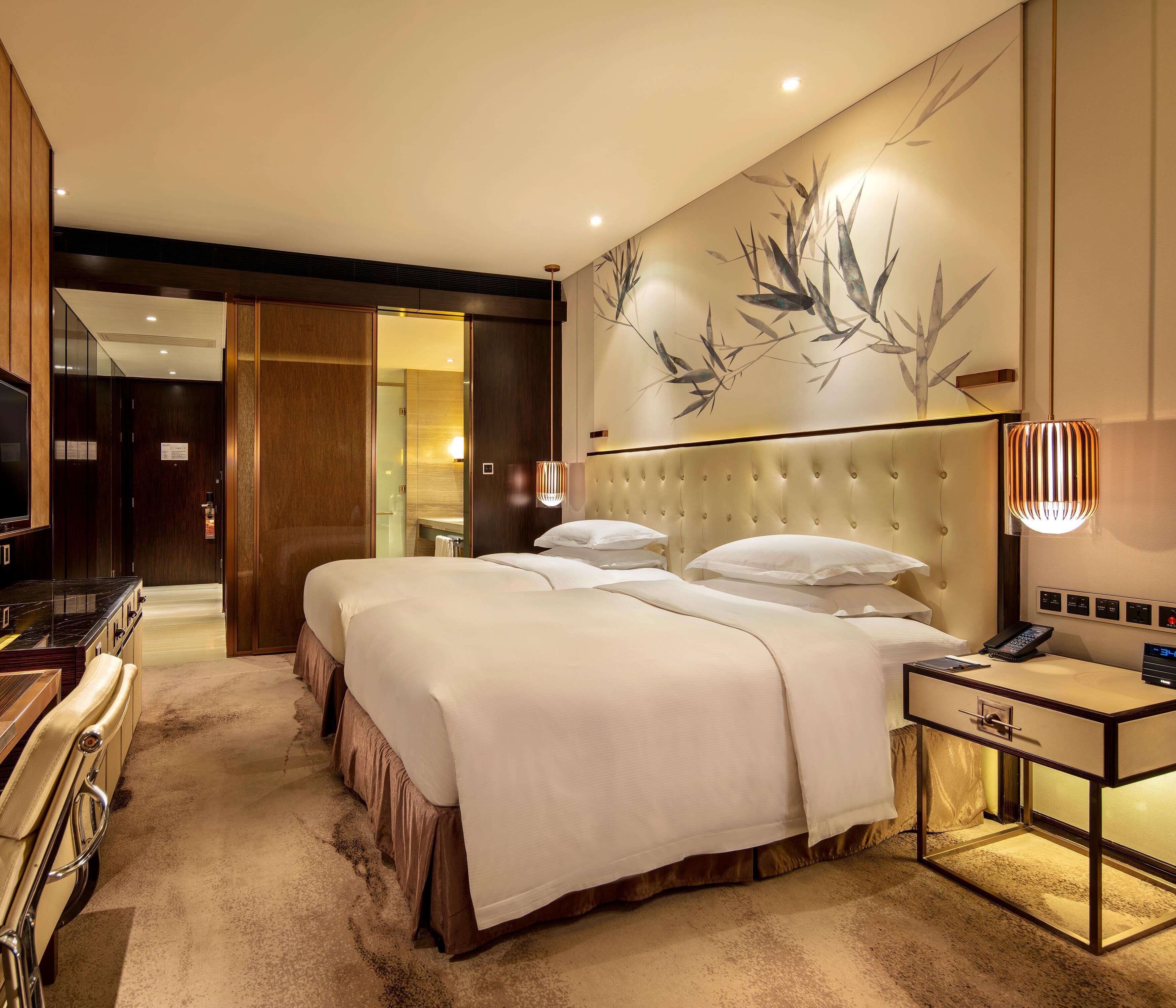 A hotel room with a large bed, bedside table, TV, and a bathroom visible through an open door.