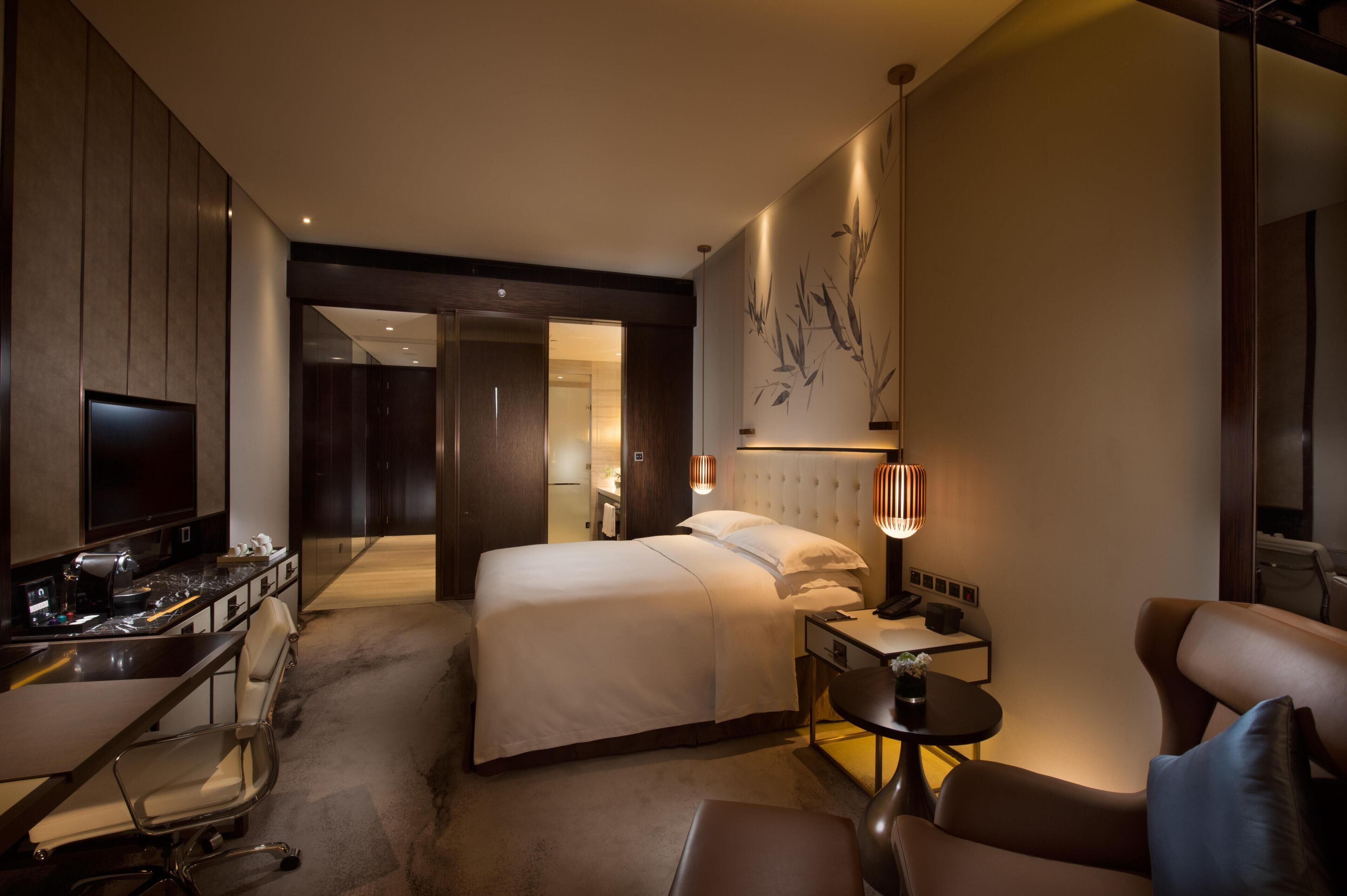 A hotel room with a bed, desk, chair, and a TV.