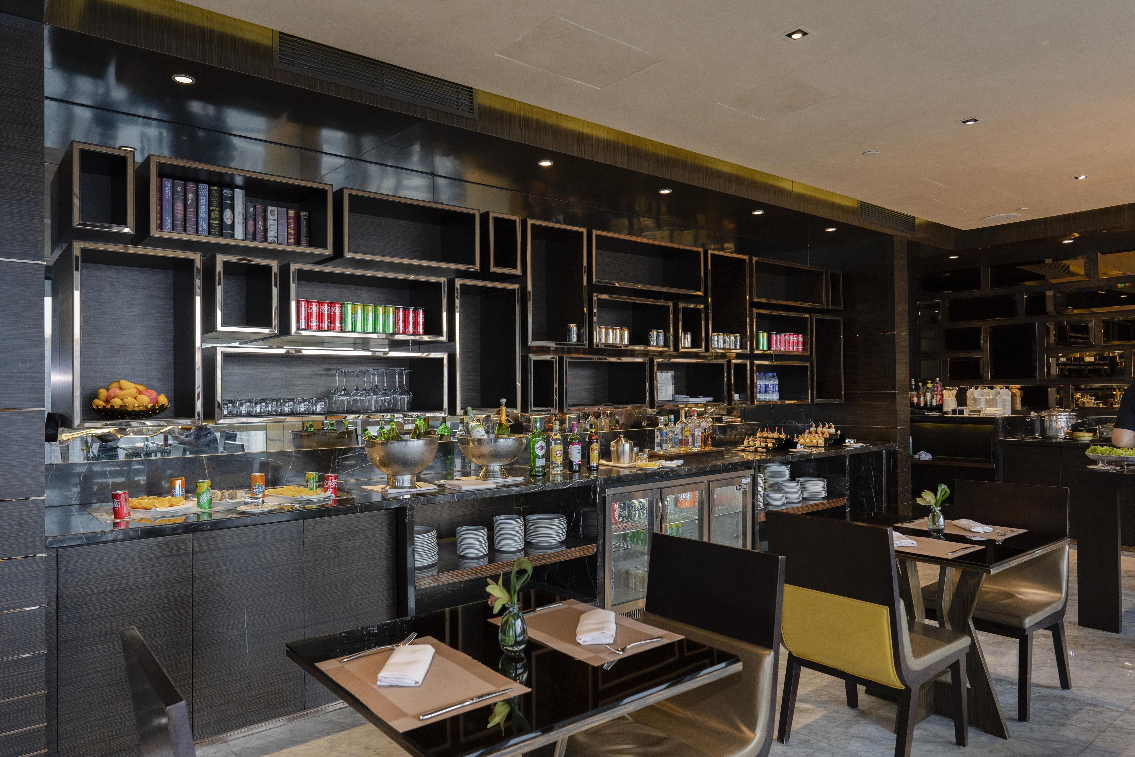 Een moderne bar met drankenkasten, een buffet met borden en bestek, en zitplaatsen met tafels en stoelen.