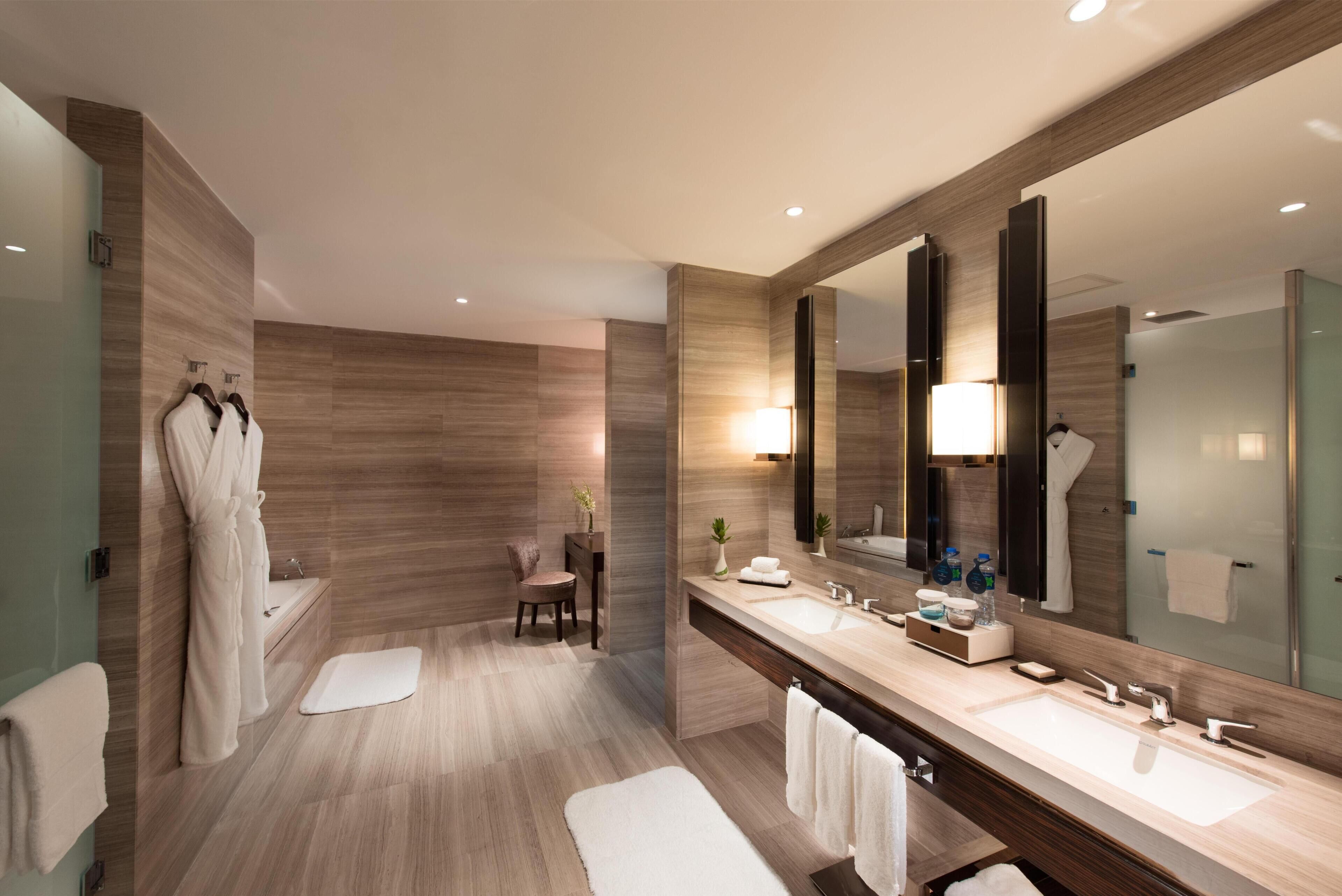 A modern bathroom with two sinks, a large mirror, and a seating area.