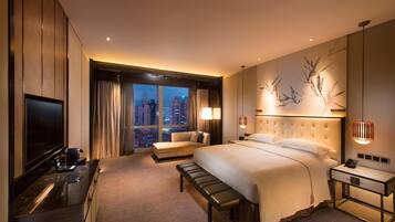 A hotel room with a large bed, a sofa, a desk with a TV, and a city view.