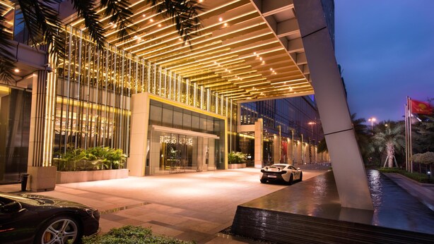 A modern building with a glass facade, a car parked in front, and a water feature. - Hilton Shenzhen Futian (Shenzhen)
