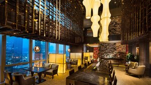 A modern hotel lobby with a large dining table, comfortable seating, a bar area, and a city view through large windows. - Hilton Shenzhen Futian (Shenzhen)