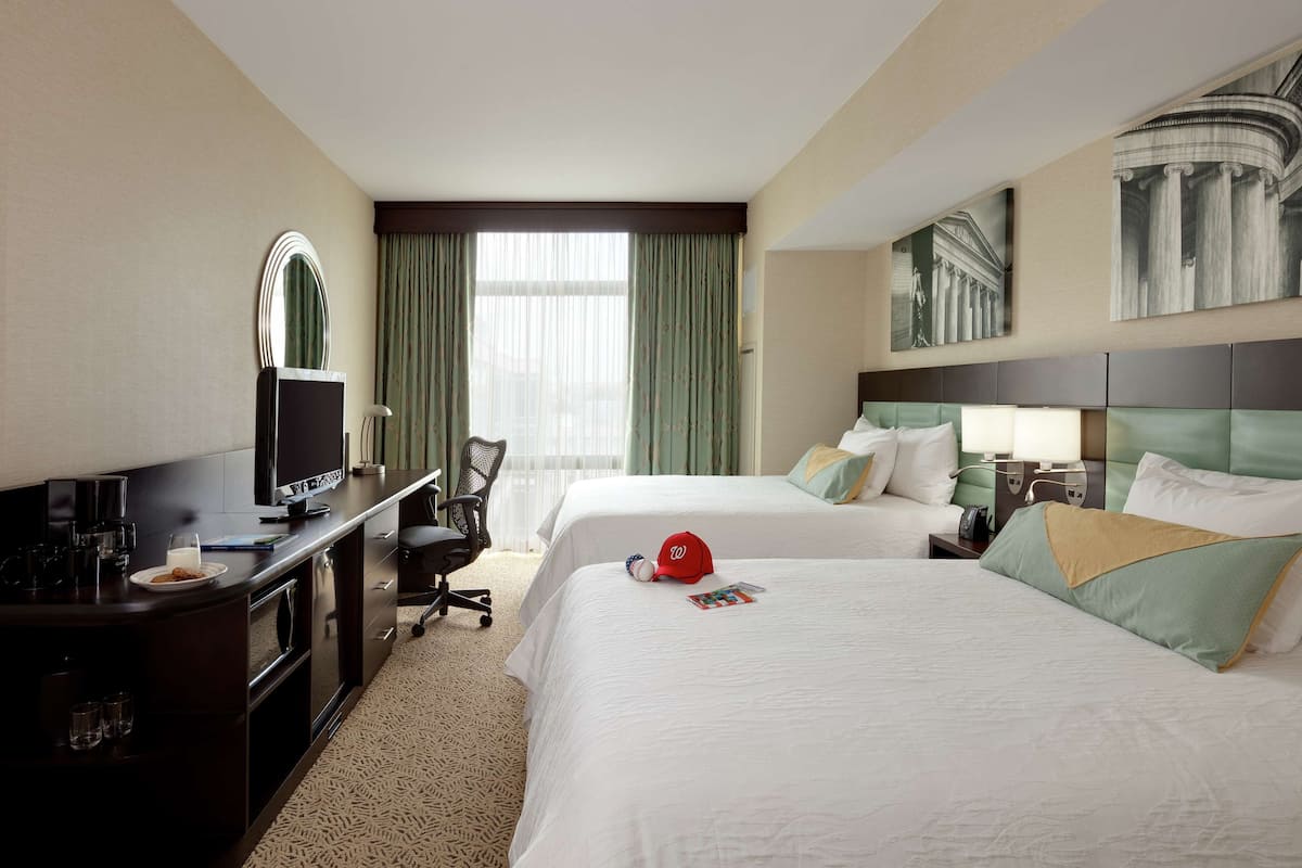 Una habitación de hotel con dos camas, un escritorio con computadora, una silla y un televisor.