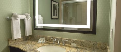Un baño con lavamanos de encimera de granito, un espejo grande y un cuadro en la pared.