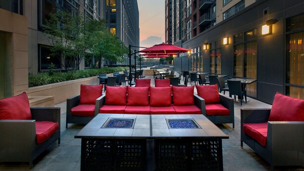 An outdoor seating area with red cushioned sofas and tables, surrounded by tall buildings. - Hilton Garden Inn Washington DC/U.S. Capitol (Washington)