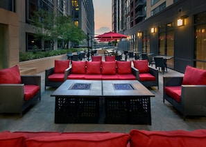 An outdoor seating area with red cushioned sofas and tables, surrounded by tall buildings. - Hilton Garden Inn Washington DC/U.S. Capitol (Washington)