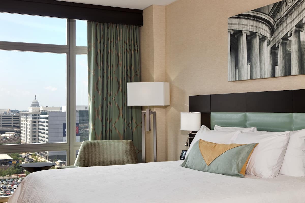 Habitación de hotel con una cama grande, vistas a la ciudad, una silla verde y un cuadro en la pared.