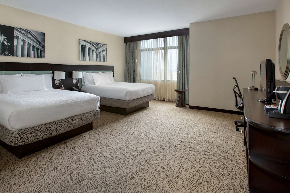 Una habitación de hotel con dos camas, un escritorio, una silla, una lámpara y un espejo grande.