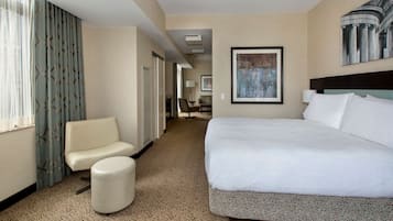 Una habitación de hotel con una cama grande, un sofá, un reposapiés y vistas al pasillo.