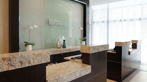 A modern hotel reception area with a glass wall displaying the Hilton Garden Inn logo, a marble counter, and potted plants. - Hilton Garden Inn Washington DC/U.S. Capitol (Washington)