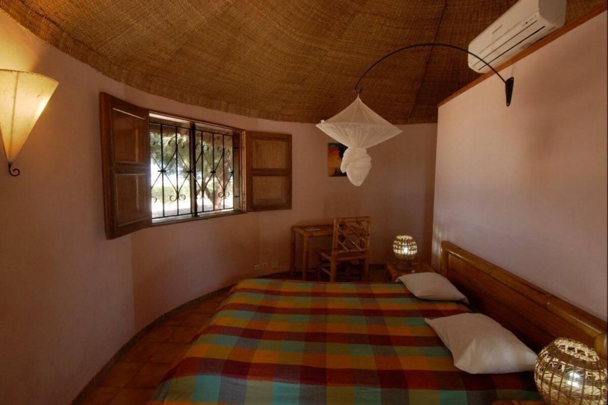 Ein Zimmer mit einem Bett, einem Sessel, einem Tisch, einem Fenster und einer Klimaanlage.