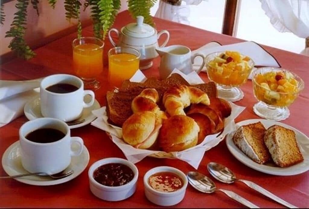 Una mesa de desayuno con panecillos, fruta, café y té.
