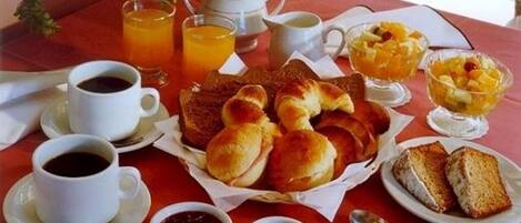 Una mesa de desayuno con panecillos, fruta, café y té.