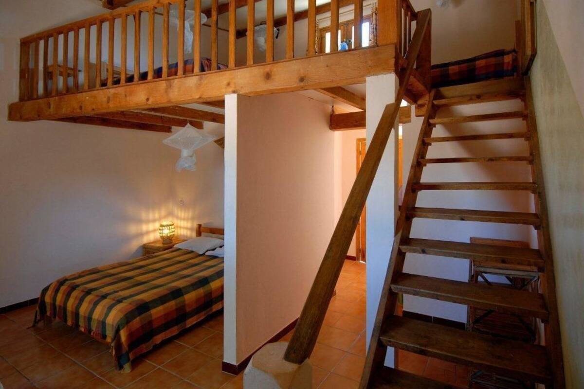Ein Schlafzimmer mit einer Holztreppe, einem Bett mit gestreifter Decke und einem Nachttisch mit Lampe.