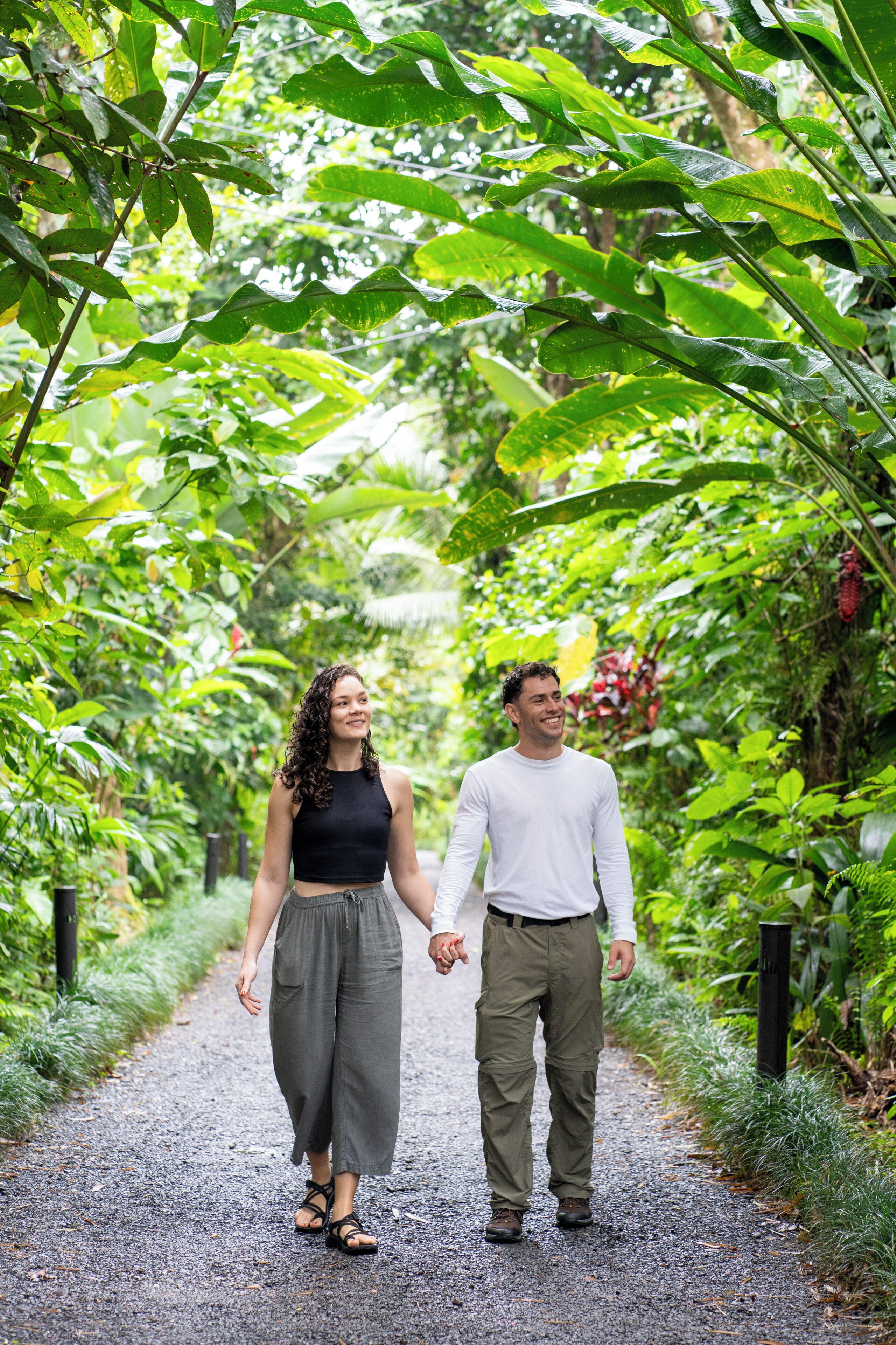 Two people walking on a gravel path surrounded by lush greenery.