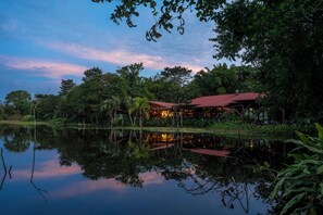 A lakeside lodge with a red-roofed building surrounded by lush greenery and a calm reflective water surface. - Maquenque Lodge (Pital)