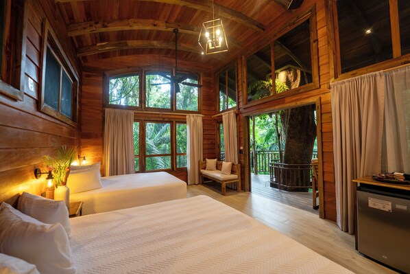 A cabin with two beds, a dining area, and a balcony with a view of the forest. - Maquenque Lodge (Pital)