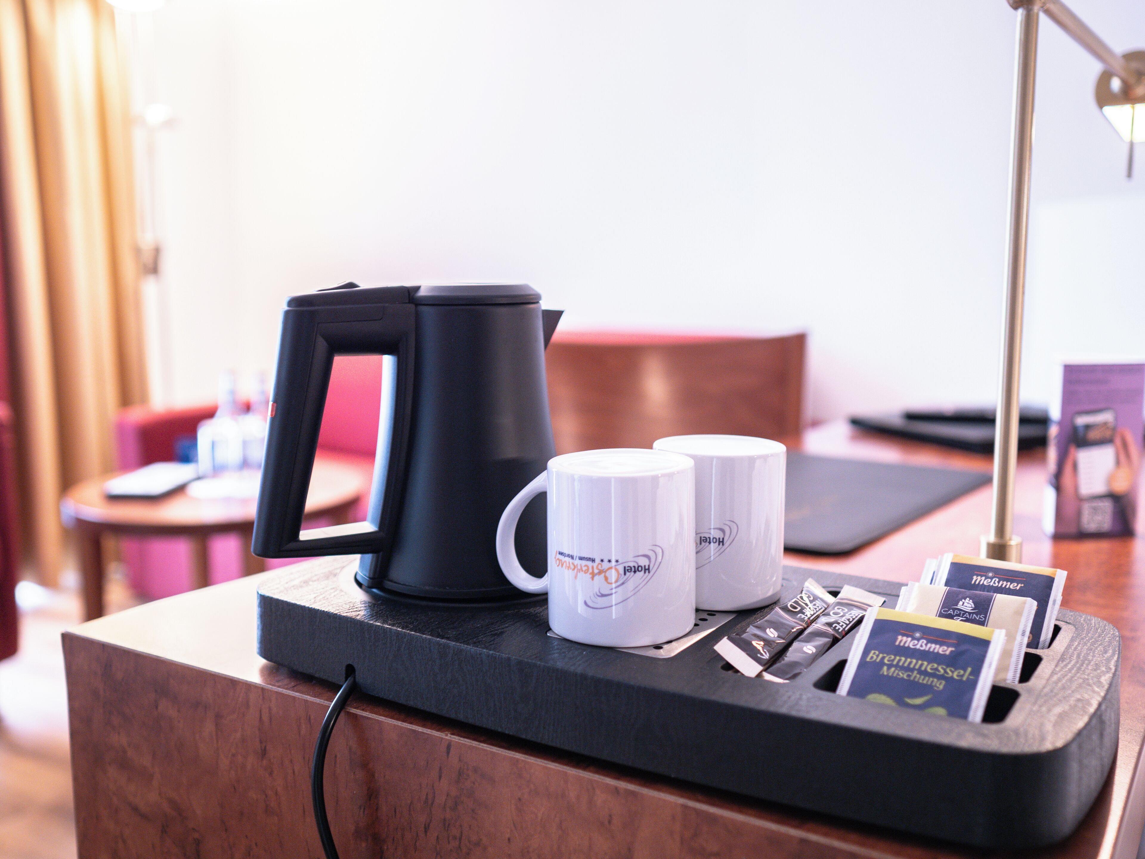 Een hotelkamer met een koffiezetapparaat, twee witte mokken en een dienblad met theezakjes en een brochure.