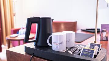 Een hotelkamer met een koffiezetapparaat, twee witte mokken en een dienblad met theezakjes en een brochure.