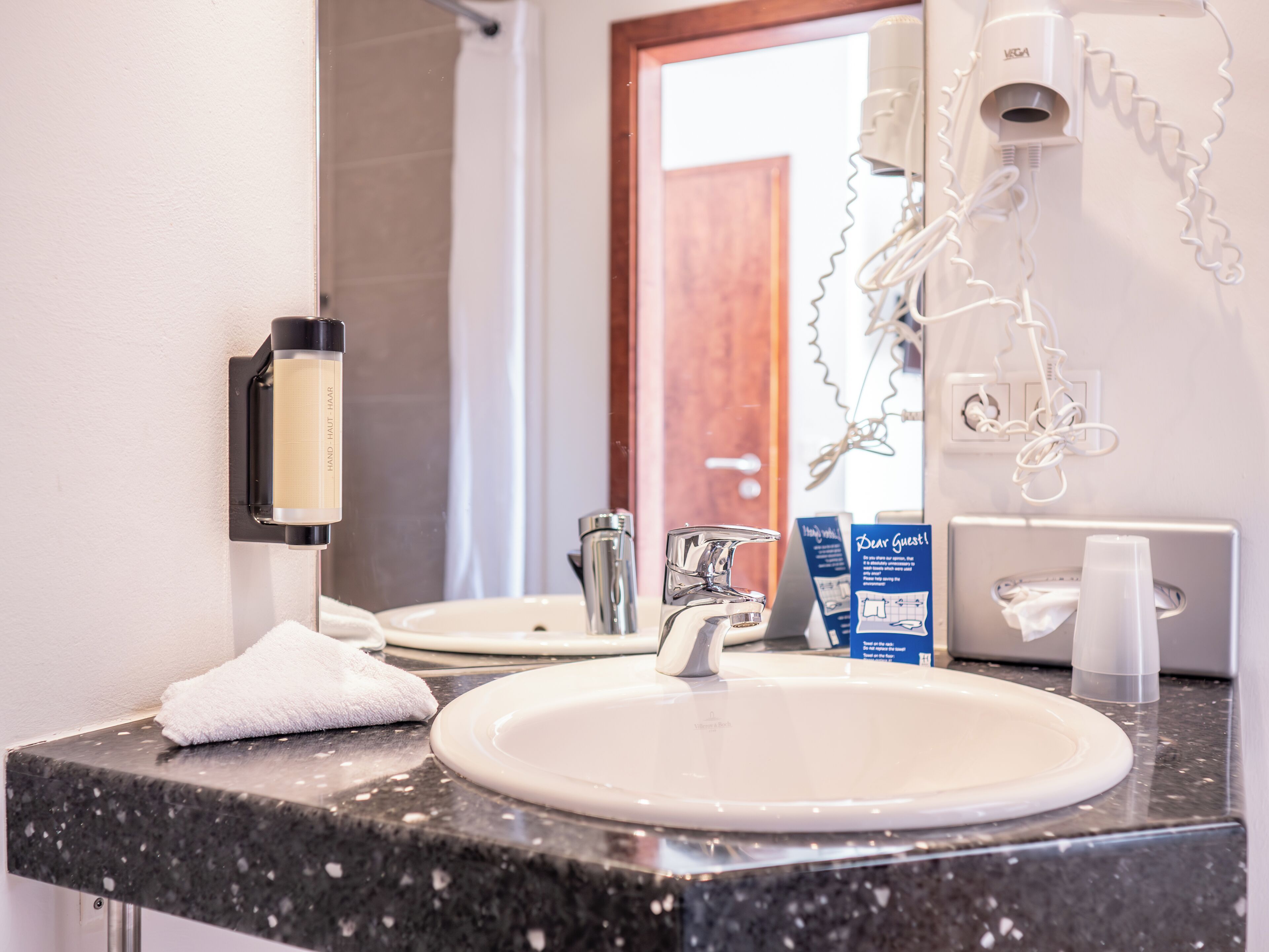 A bathroom with a sink, mirror, towel, and a hairdryer mounted on the wall.