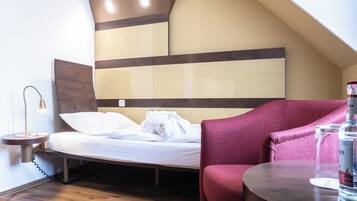 A hotel room with a bed, a red chair, a small table, and a bottle of water.