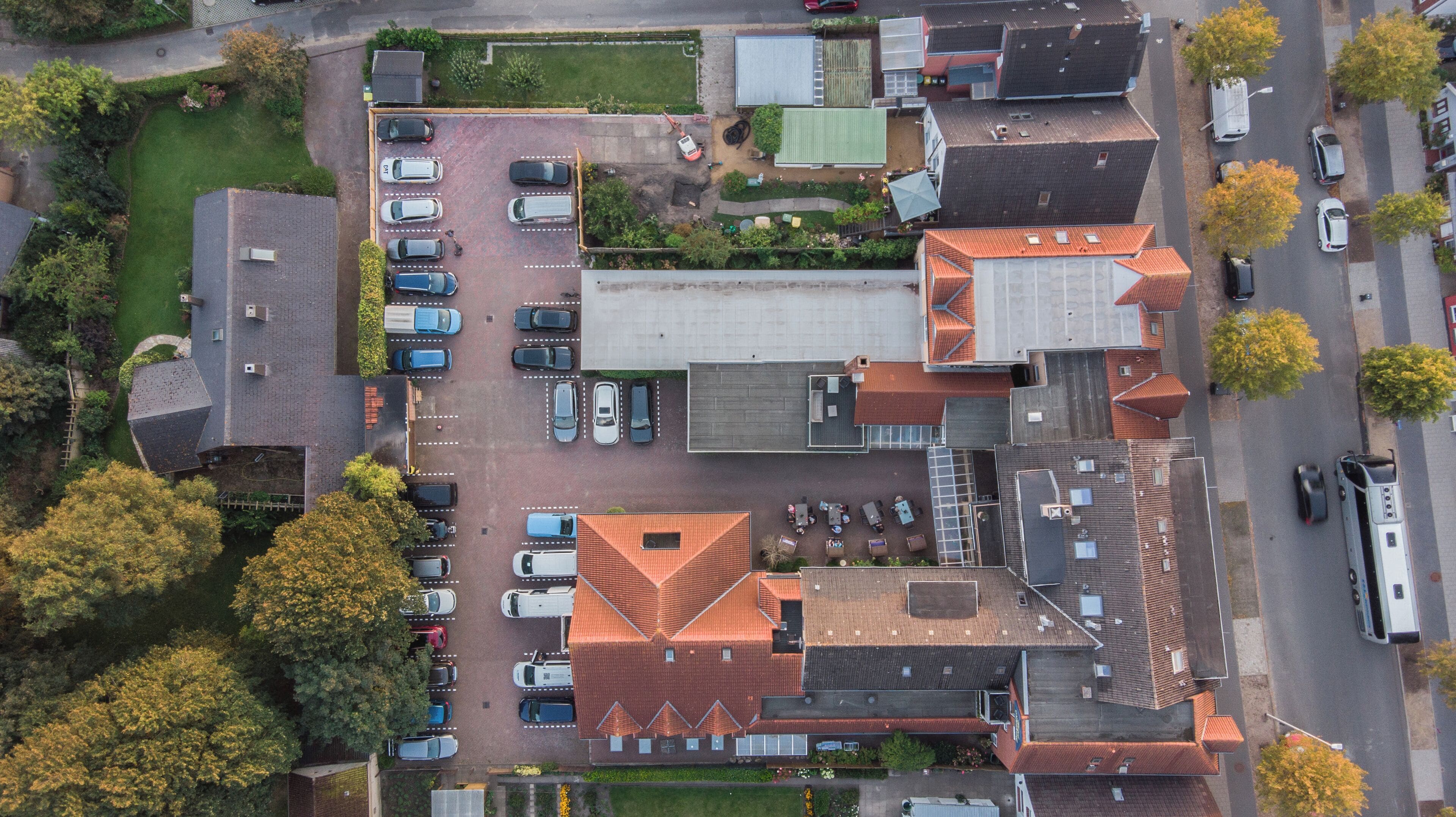 An aerial view of a residential area with multiple houses, a parking lot, and a few vehicles.