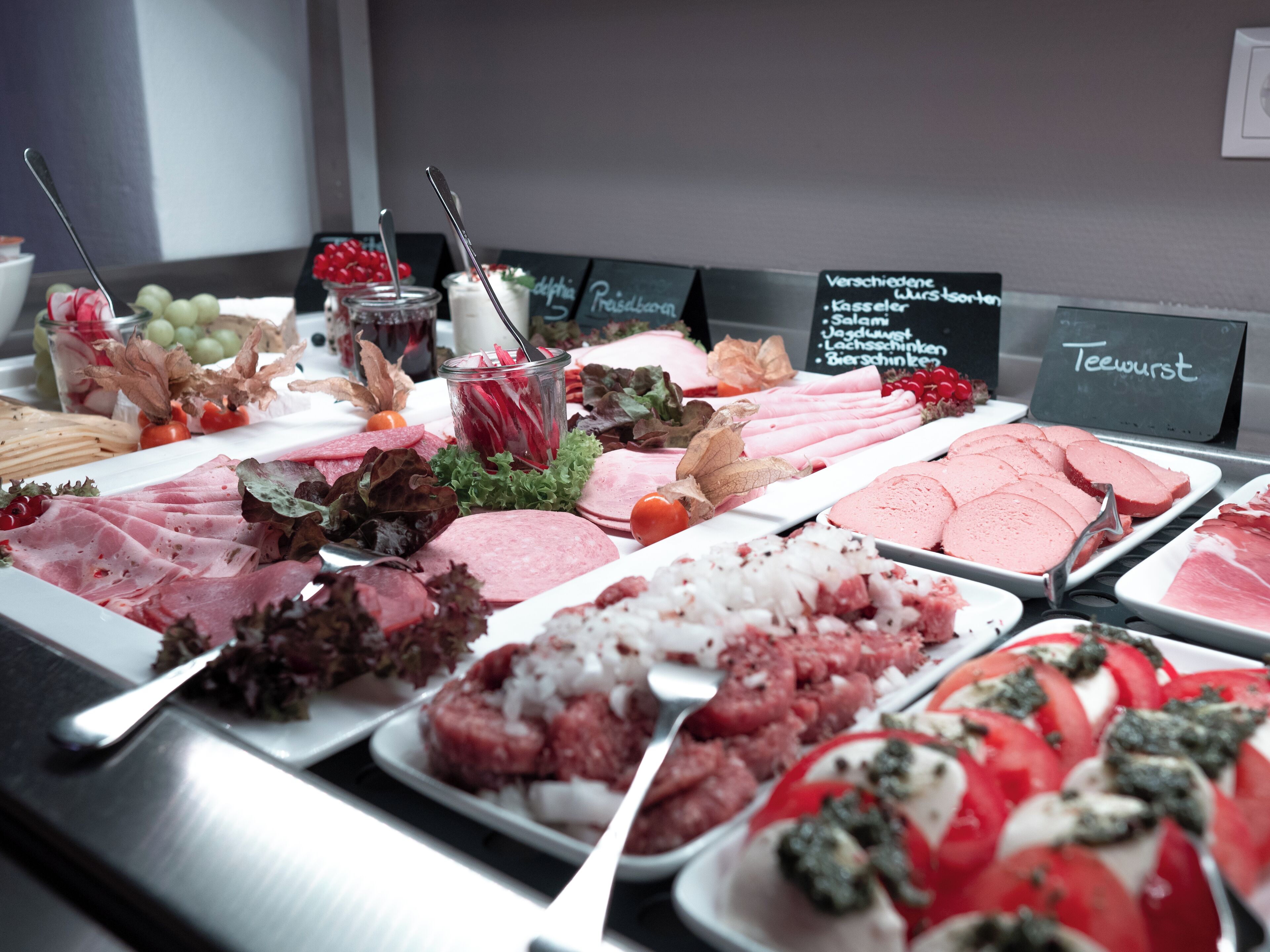 A variety of meats and cheeses displayed on a buffet table with labels indicating different types.